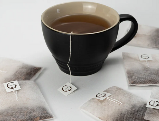 Philippine Cacao Chocolate Tea in a black mug and loose tea bags on a white surface