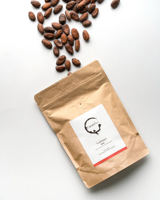 A paper pouch laid flat labeled 'Peru - Trailblazer' with scattered whole Peruvian cacao beans spilling from the top