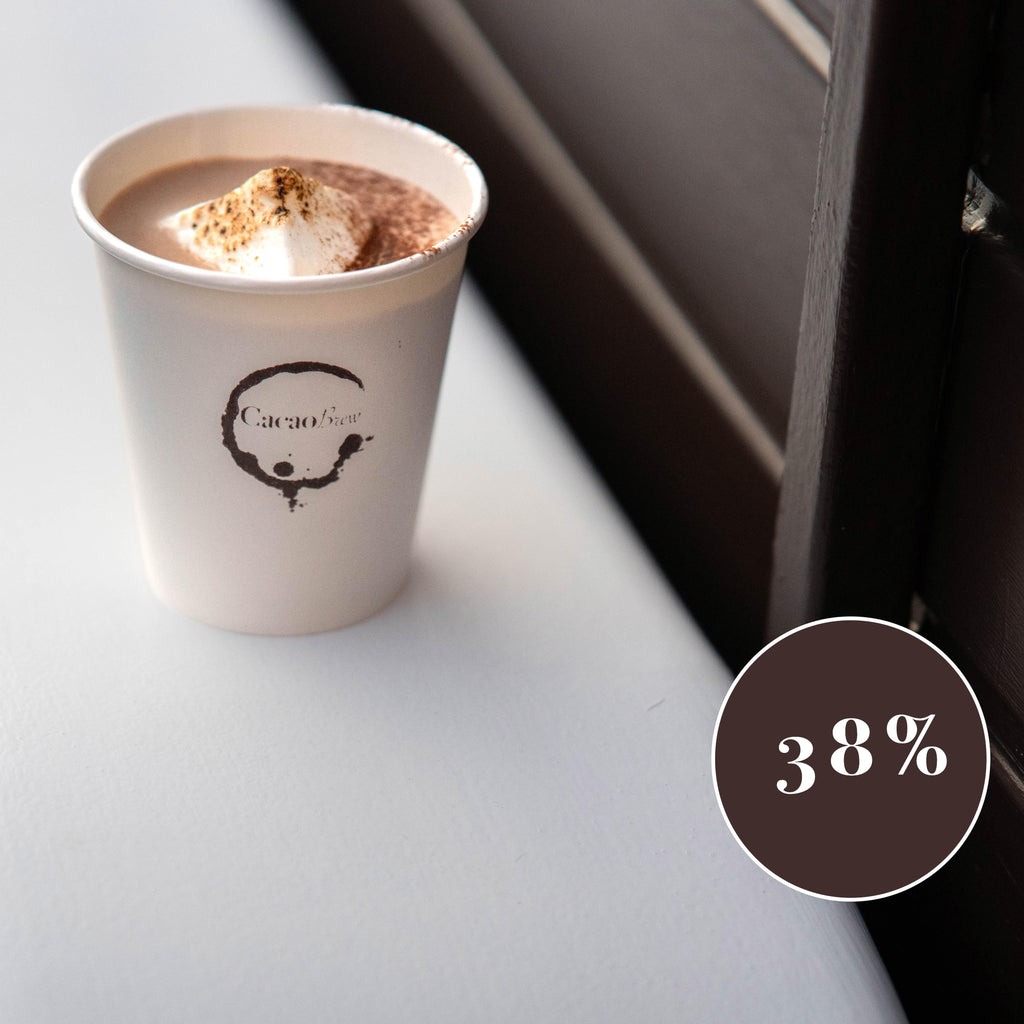 Close up of a cacao brew branded paper cup containing luxury organic hot chocolate and a mega mallow. Cup is placed on the mudguard of the Cacao Brew drinks trailer. A circular sign shows 38% which indicates the percentage of cacao powder in this drink.