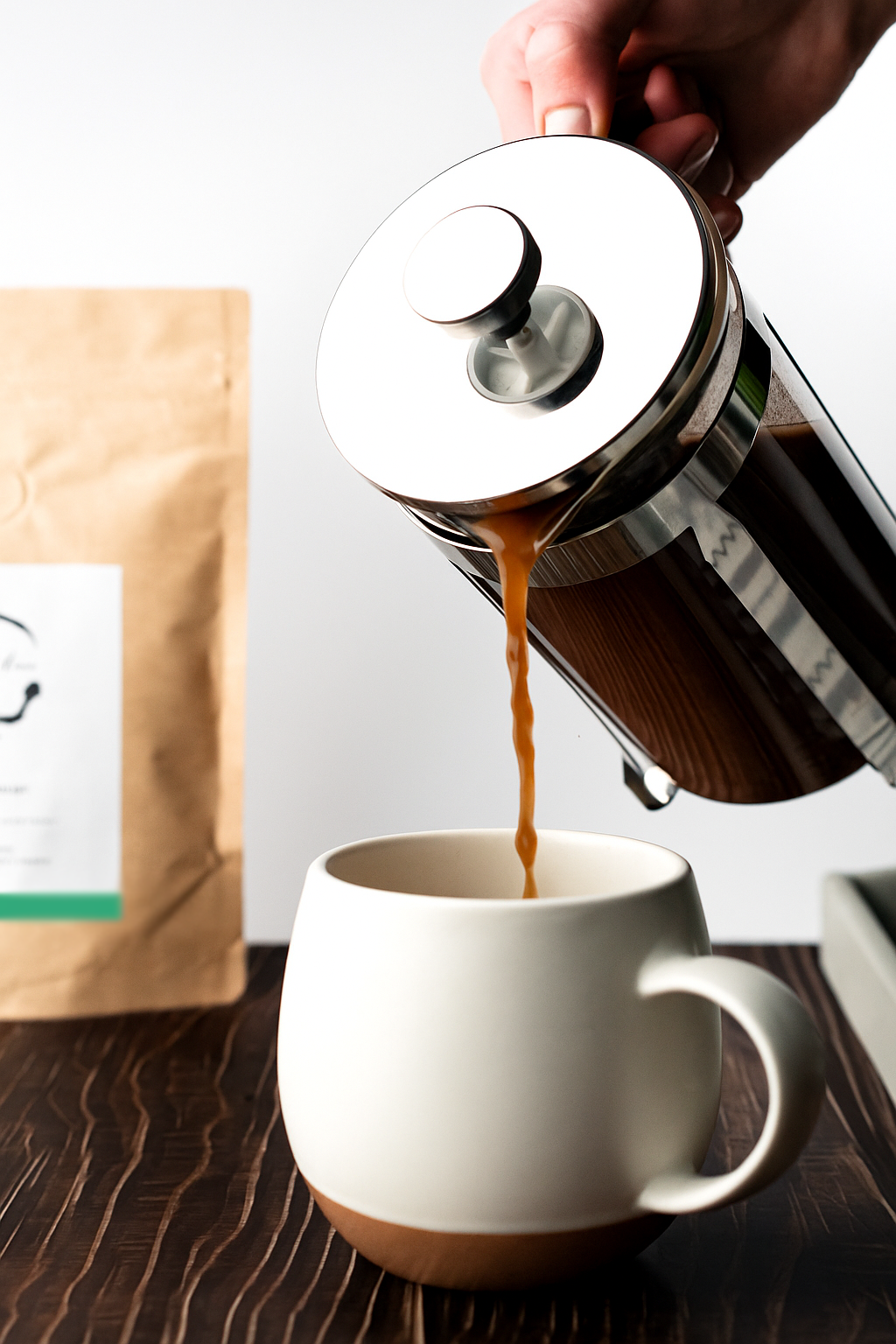 Brewing Cacao being poured from a French press into a white mug on a wooden surface.