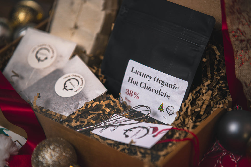 Gift set containing  1 x 150g bag of Luxury Organic Hot Chocolate, 1 x Pack of Vanilla Bean Gourmet Marshmallows, 1 x Mini Stainless Steel Whisk, 1 x 20g Sachet of Peruvian Brewing Cacao, 1 x Chocolate Tea bag all in a gift box with a branded gift tag. Gift box filled with brown zig zag paper