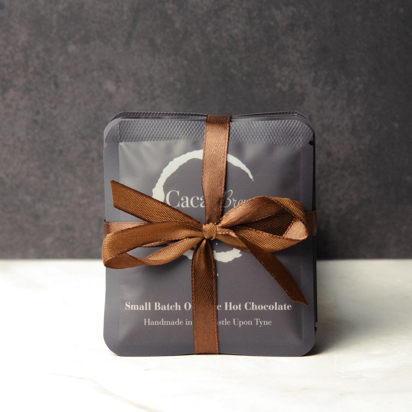 Hot Chocolate Bundle, showing five single-serve sachets of Cacao Brew organic hot chocolate tied with a bow in dark brown ribbon.