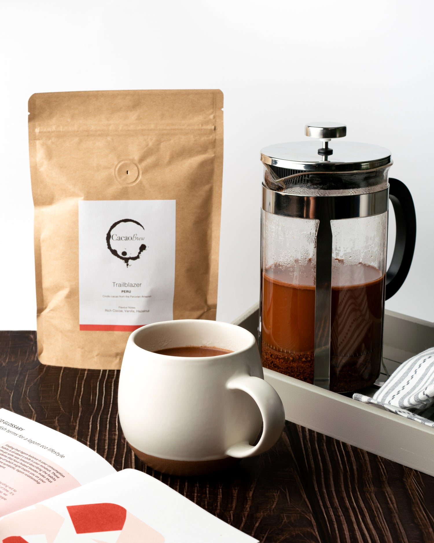 mug of Peru brewed cacao with cafetiere and a bag of Peru brewed cacao in the background